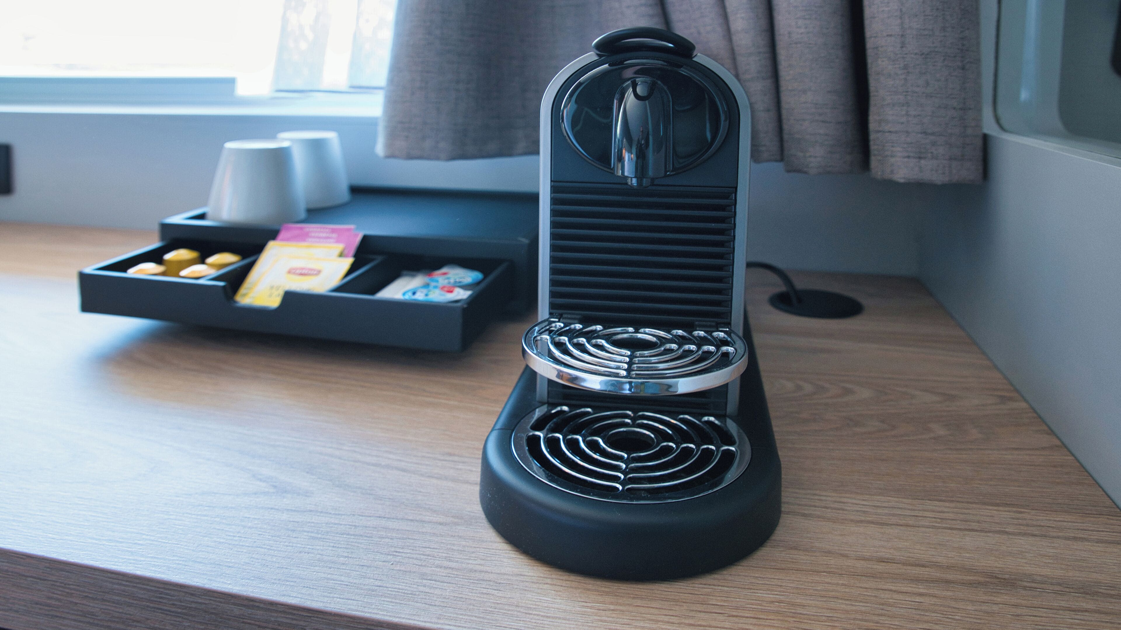 A black coffee machine with a drip tray on a wooden table.