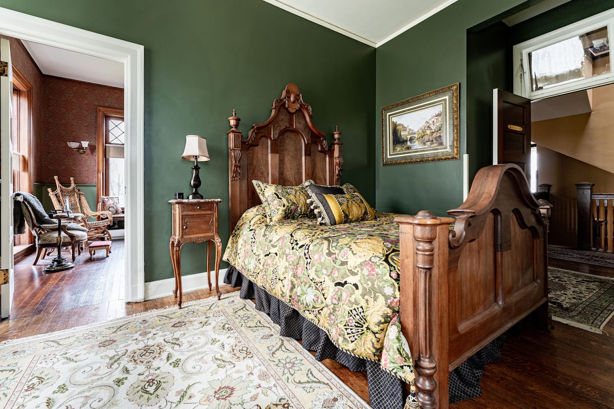 A traditional bedroom with a wooden bed, a matching nightstand, a chair, a lamp, and a large rug.
