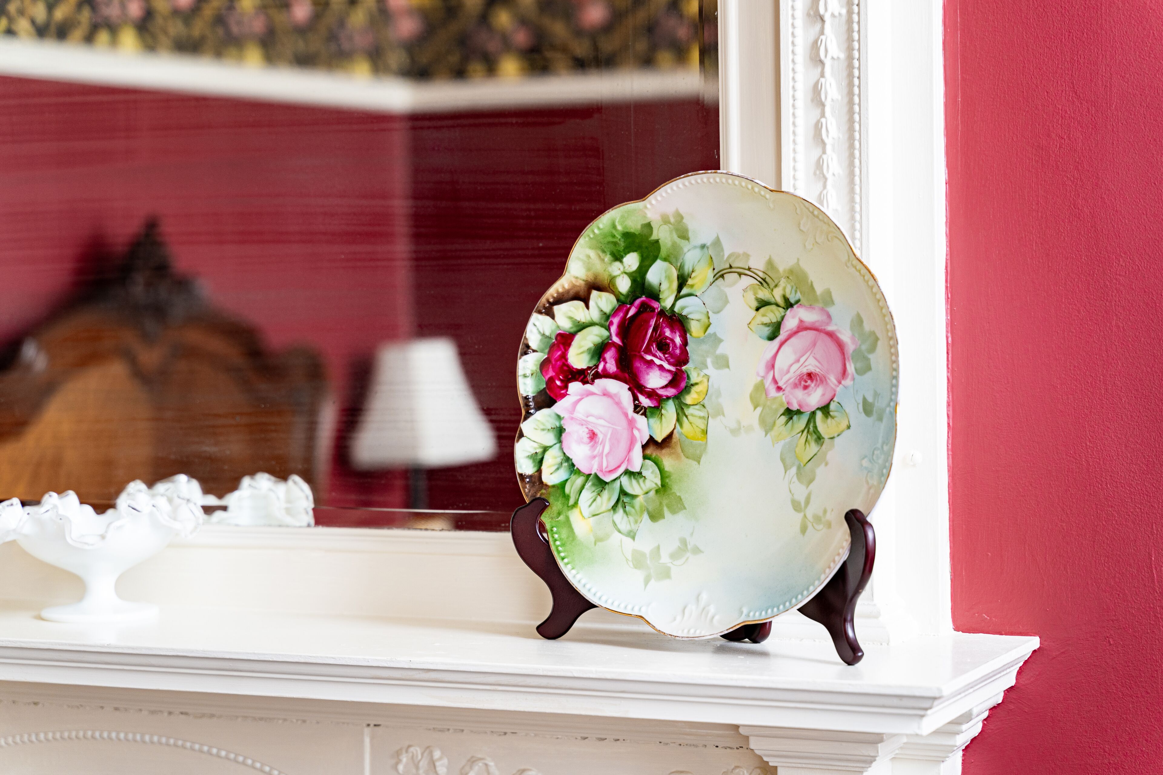 A decorative plate with floral designs on a white mantelpiece.