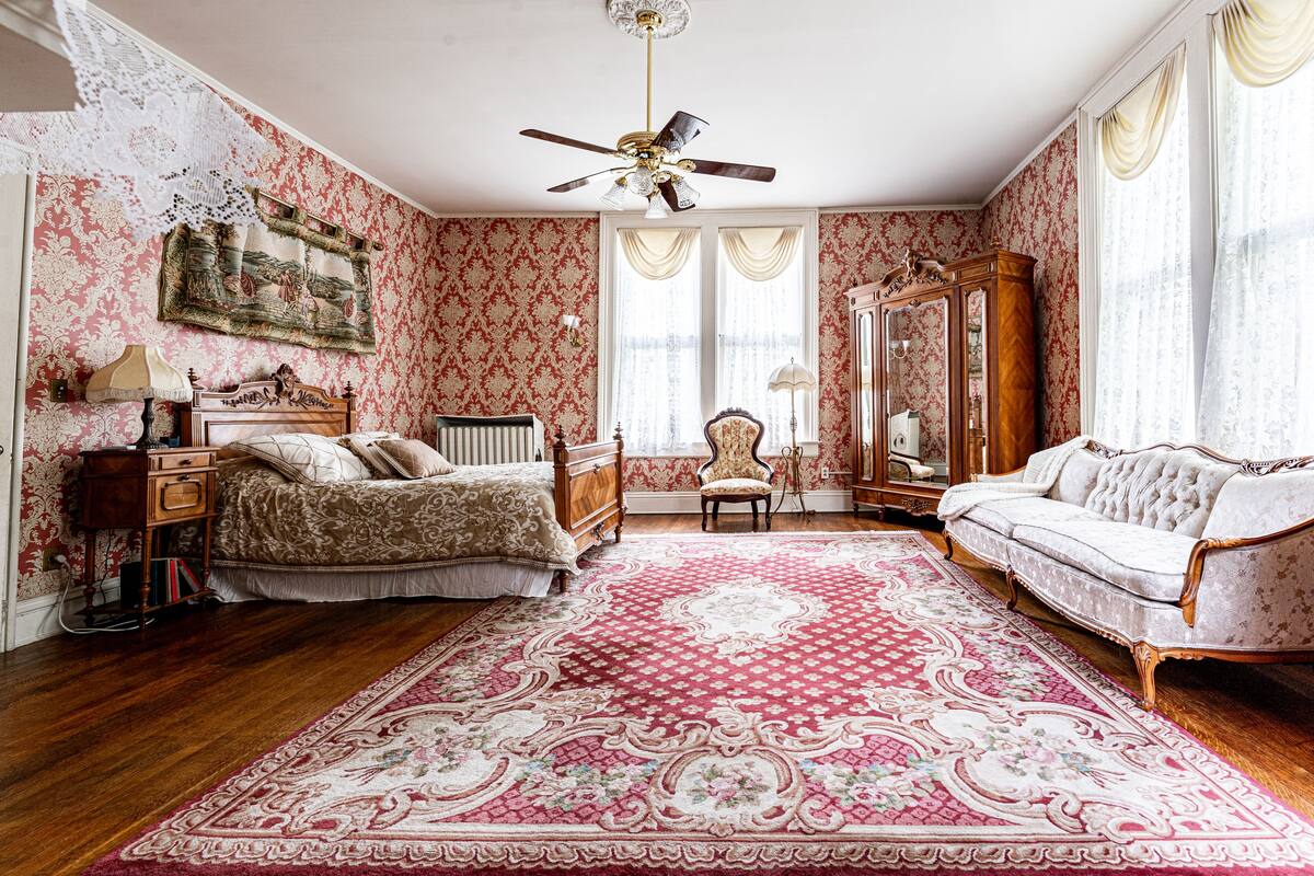 A room with a bed, a sofa, a chair, a wooden cabinet, and a ceiling fan.