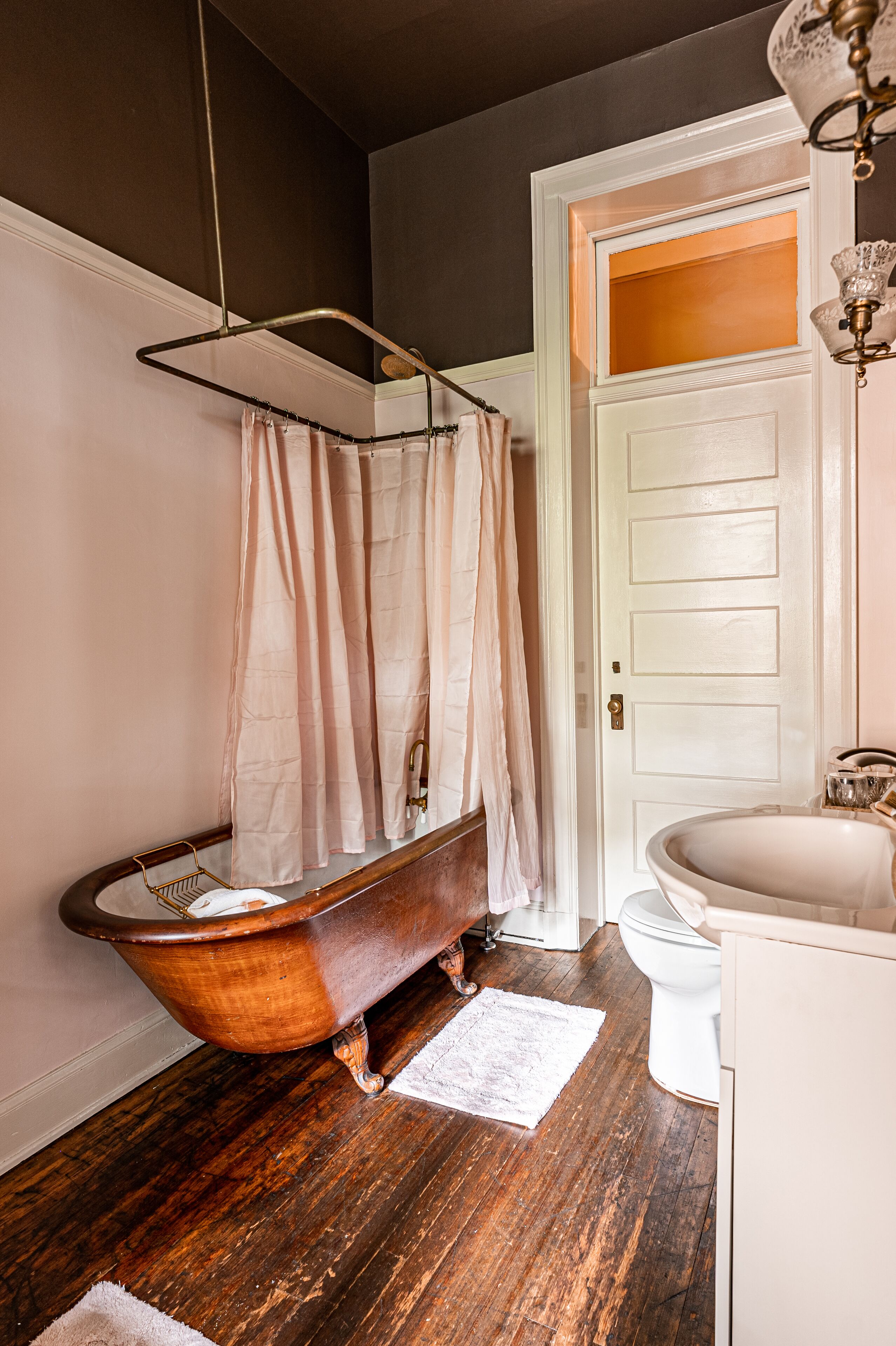 Une salle de bain avec une baignoire sur pieds, un lavabo blanc et un plancher en bois.