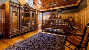 A spacious room with wooden flooring, a large ornate wooden cabinet, a bench, and a patterned rug. - Vrooman Mansion B&B (Bloomington)