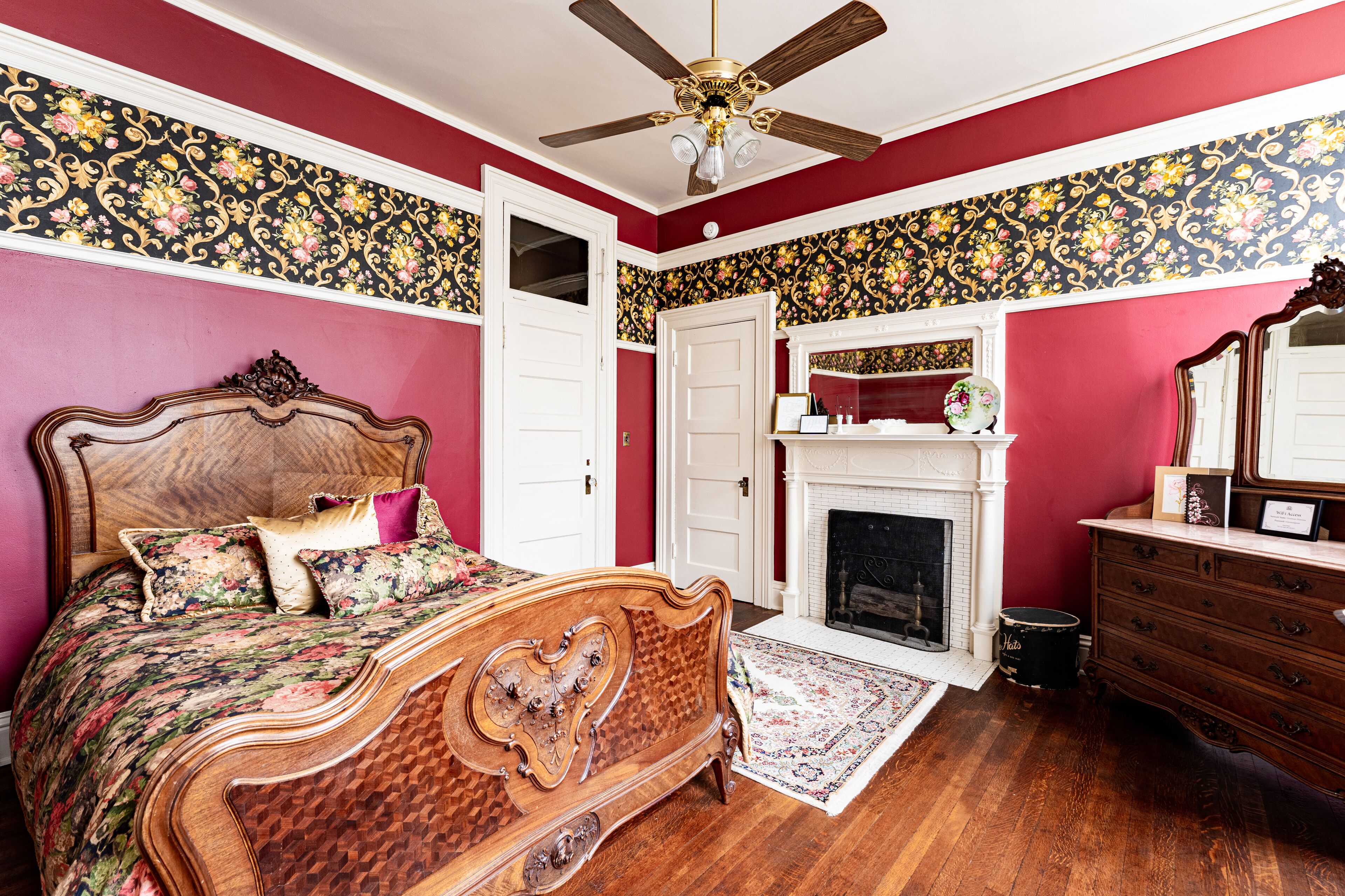 A bedroom with a wooden bed, a ceiling fan, a fireplace, and a dresser.
