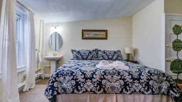Un dormitorio ordenado con una cama grande, una mesita de noche con lámpara, un espejo y un cuadro en la pared.