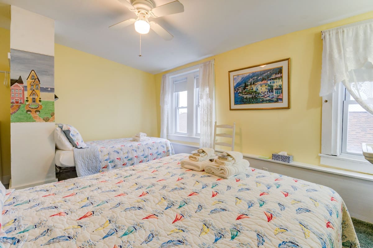 A bedroom with two beds, a ceiling fan, a painting, and a window with curtains.