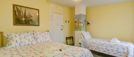 A room with two beds, each with a sailboat pattern bedspread, a ceiling fan, and a painting of a sailboat on the wall.