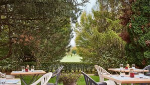 An outdoor dining area with tables and chairs, surrounded by trees and a view of a golf course. - Kyriad Direct Epinal (Epinal)