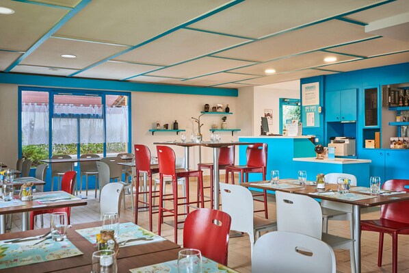 A restaurant with tables and chairs, a counter, and shelves with items. - Kyriad Direct Epinal (Epinal)