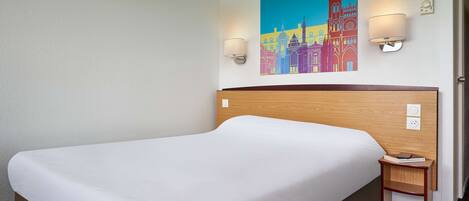 A hotel room with a large bed, a wooden headboard, two wall-mounted lamps, and a colorful cityscape painting.