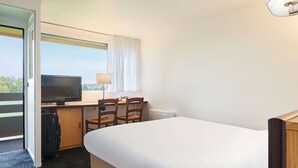 A hotel room with a bed, a desk with a television, two chairs, and a suitcase. - Kyriad Direct Epinal (Epinal)