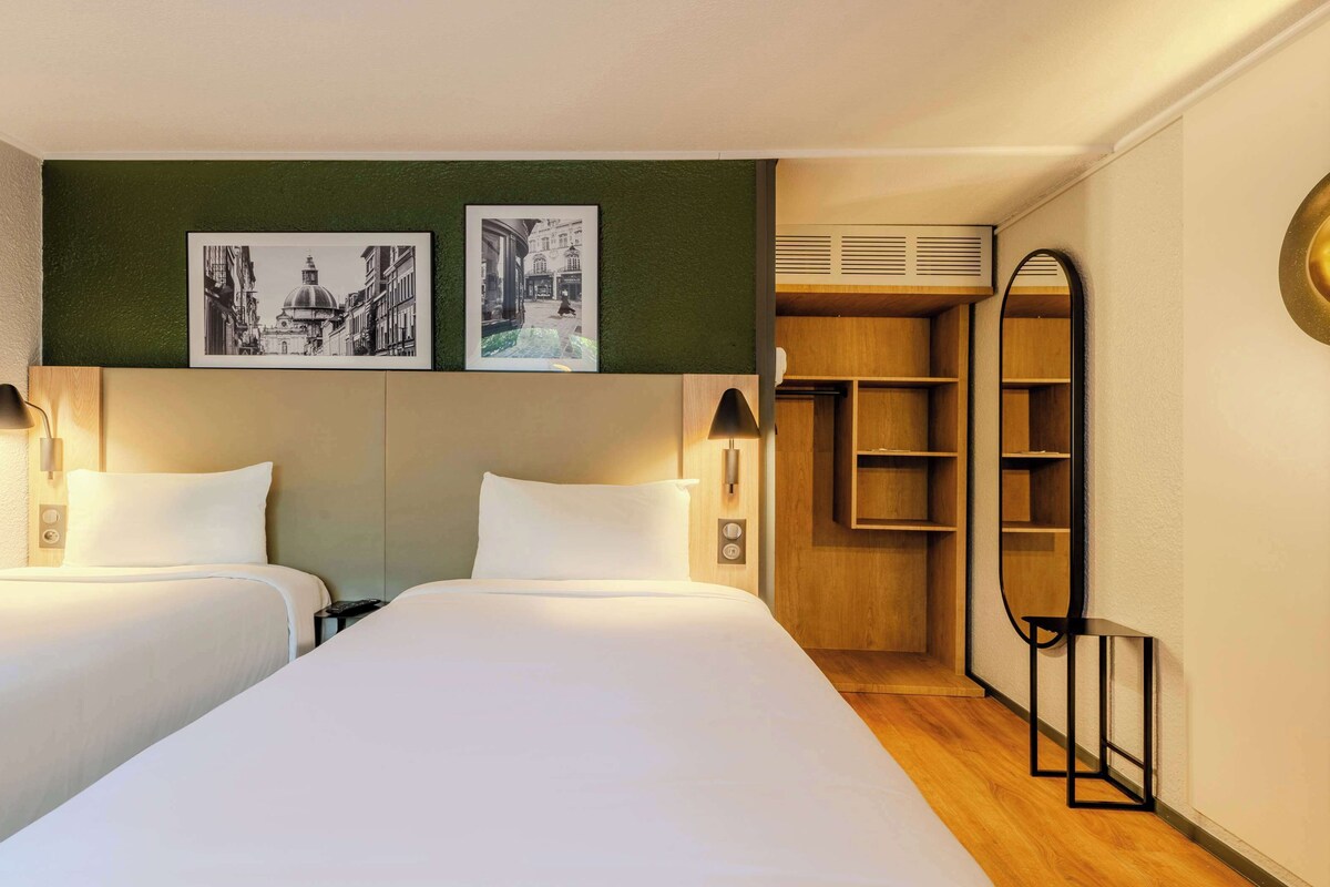 Ein Hotelzimmer mit zwei Betten, einem Holzkopfstück, einer grünen Akzentwand und zwei gerahmten Bildern.