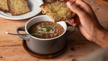 Une main tenant un morceau de pain au-dessus d’un bol de soupe, avec une cuillère à proximité.