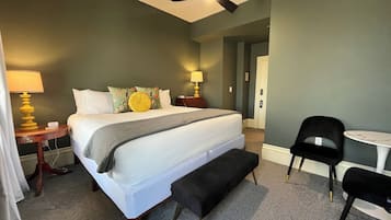 A hotel room with a large bed, bedside lamps, a bench, a small table, and a chair.