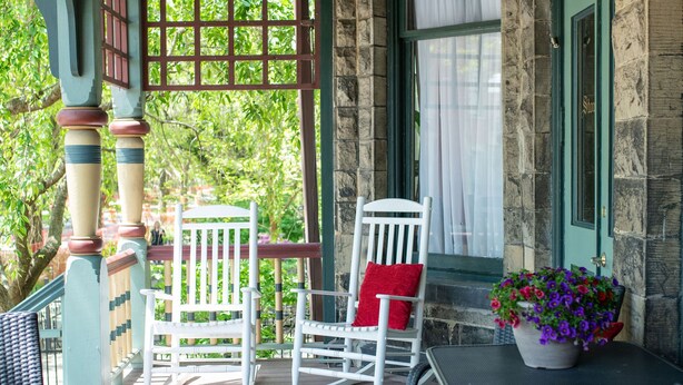 A covered porch with a wooden table and two chairs, one with a red cushion. - Stone Gables Inn (Cleveland)