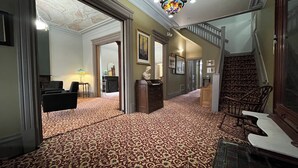 A spacious hallway with patterned carpet, a staircase, and a dining area with a table and chairs. - Stone Gables Inn (Cleveland)