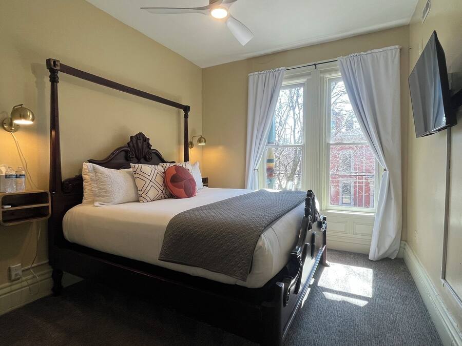 A four-poster bed with a wooden frame, a bedside table with a lamp, and a window with curtains.