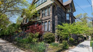 A two-story stone house with a balcony, surrounded by a black iron fence and lush greenery. - Stone Gables Inn (Cleveland)