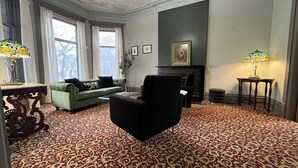 A living room with a patterned carpet, a green sofa, a black armchair, a fireplace, and two lamps. - Stone Gables Inn (Cleveland)