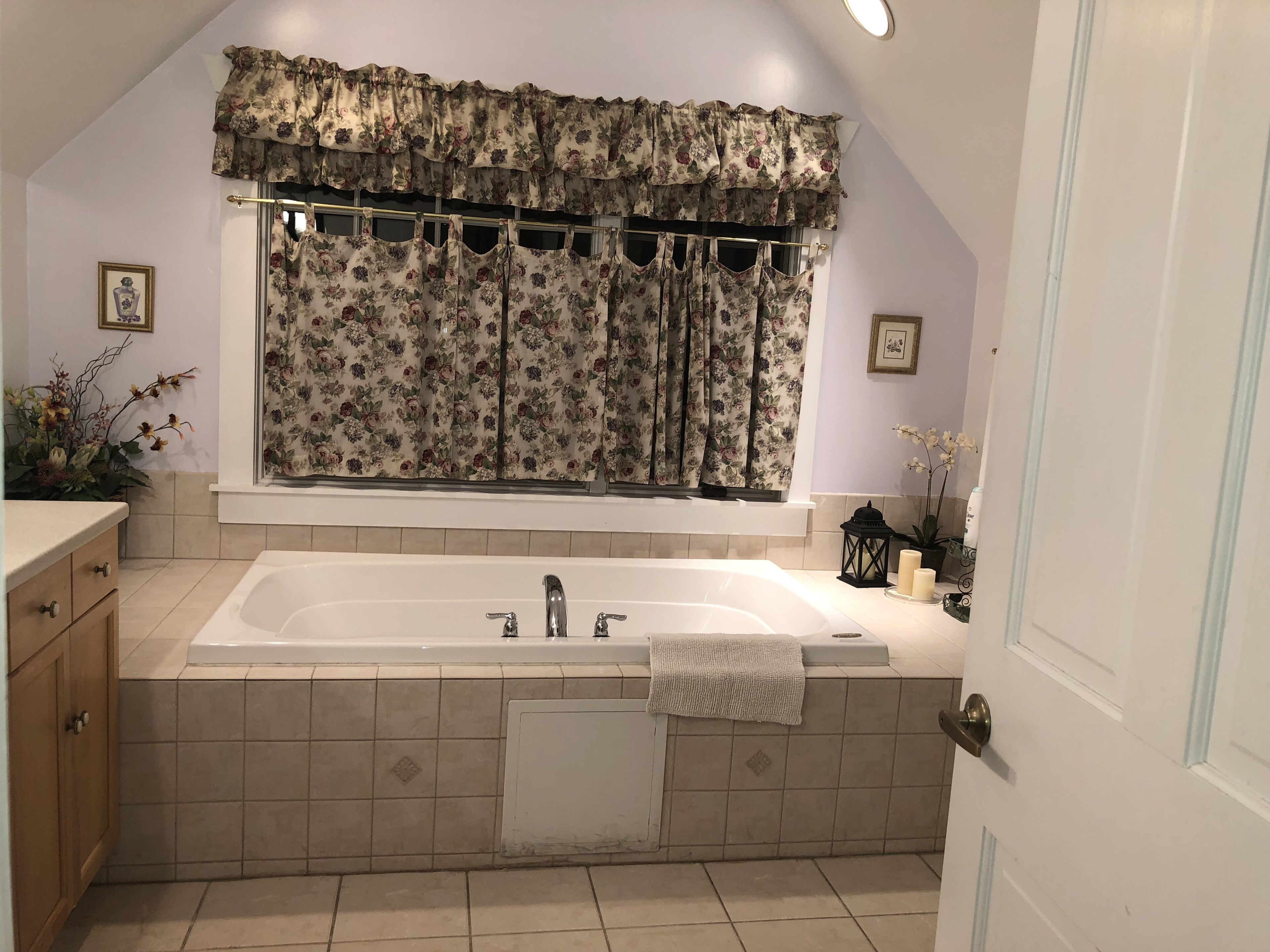 Un baño con una bañera grande, una ventana con cortinas florales, un lavabo y un espejo.