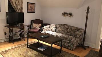 Un salon avec une table basse en bois foncé, un canapé à motifs floraux, un fauteuil en bois, un téléviseur et un porte-manteau.