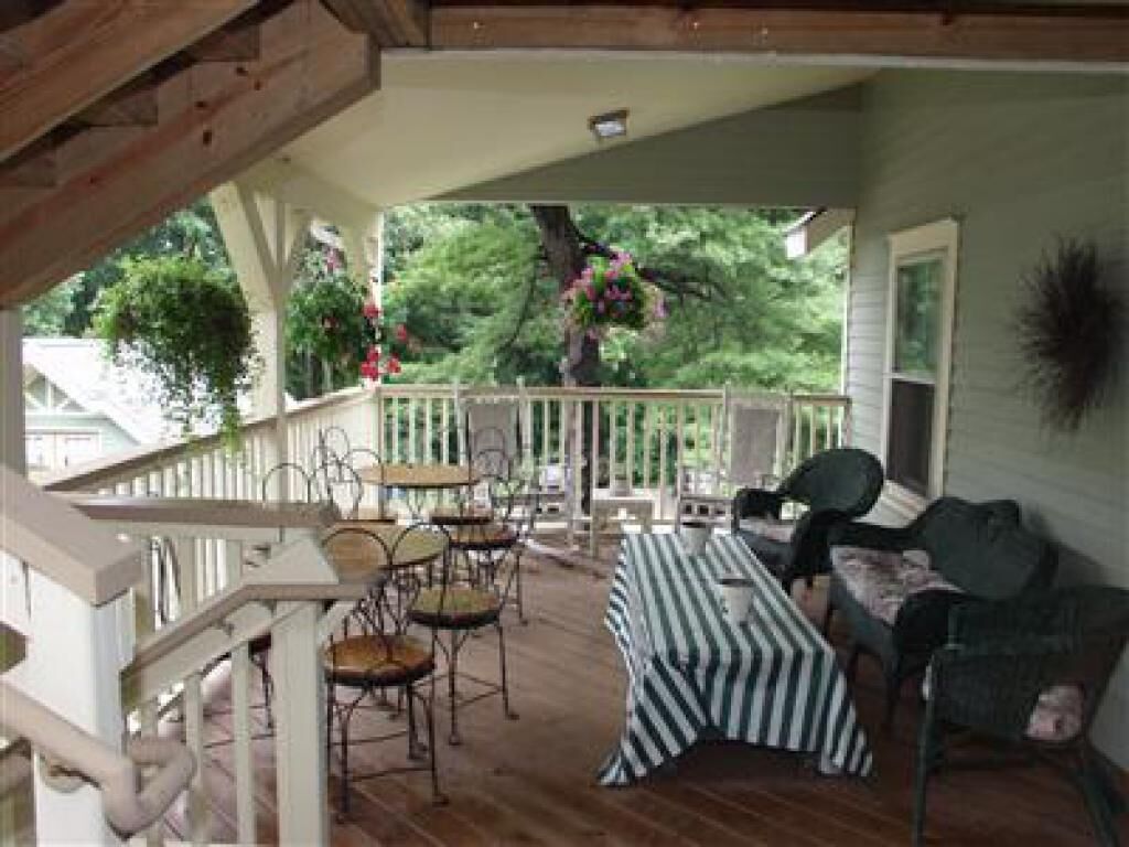 A covered porch with outdoor seating, a staircase, and a view of greenery.