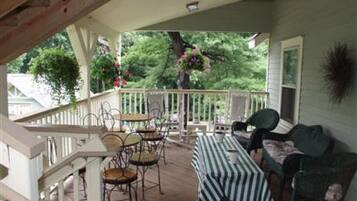 A covered porch with outdoor seating, a staircase, and a view of greenery.