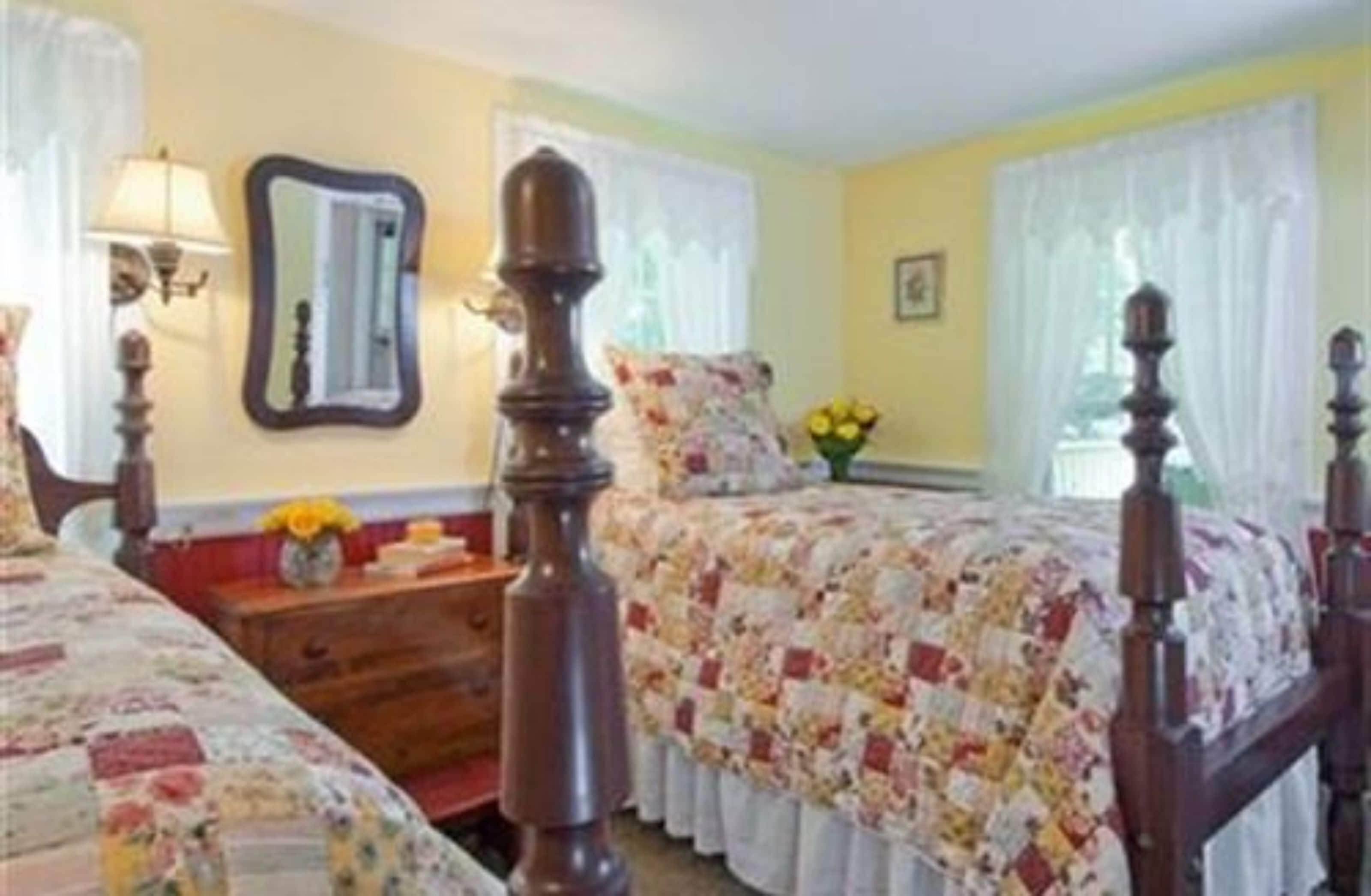 A bedroom with two beds, a wooden headboard, a nightstand, a mirror, and a window with curtains.