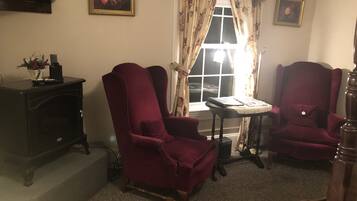 Una sala de estar con dos sillones rojos, una mesita, un aparador de madera oscura y una ventana con cortinas florales.
