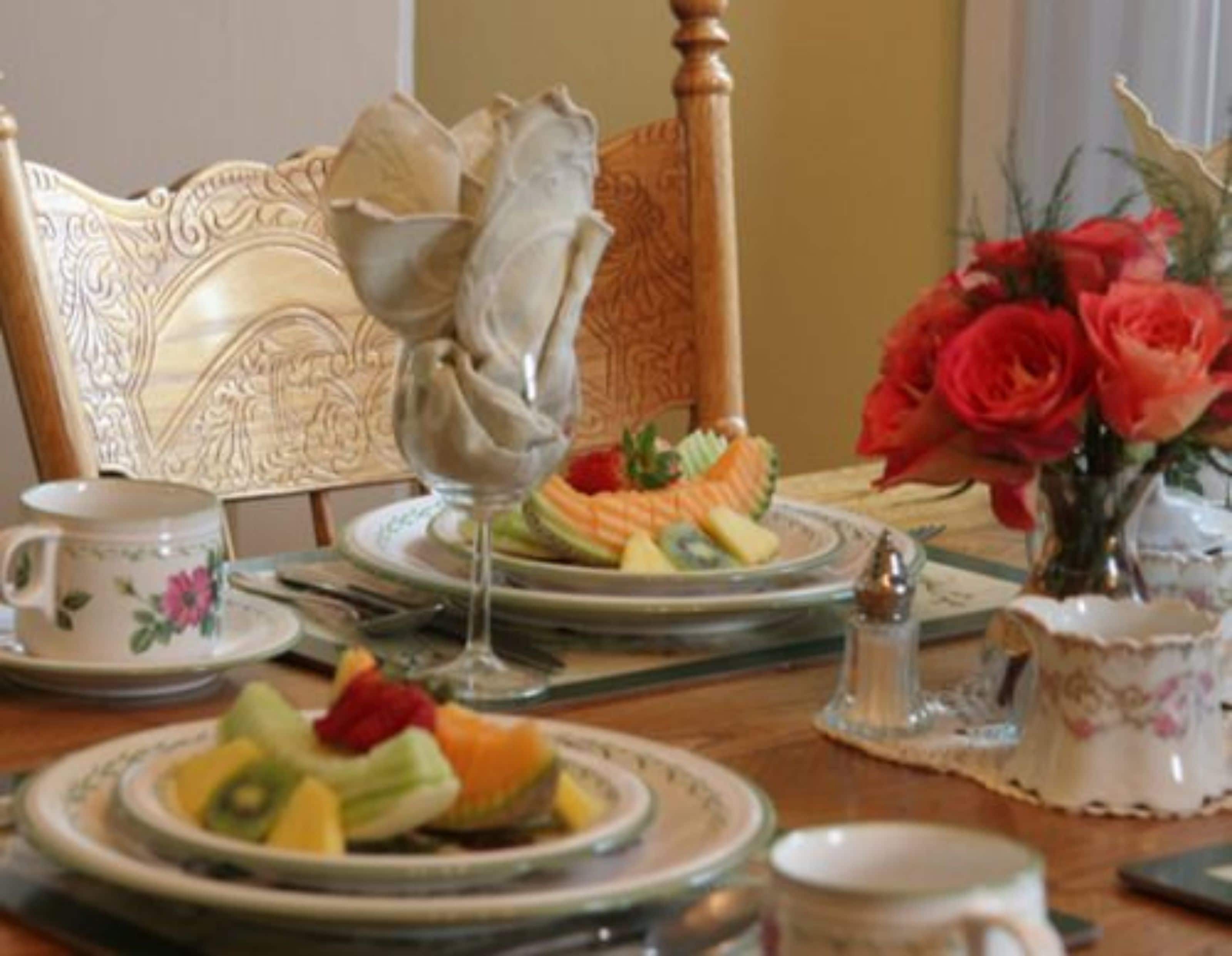 A dining table set with plates of fruit, a pitcher, and a vase with flowers.