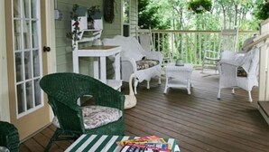A covered porch with white wicker furniture, a swan decoration, and a table with books. - Alpine Haus Bed & Breakfast Inn (Vernon)