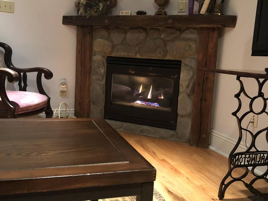 A cozy living room with a stone fireplace, a wooden dining table, and a patterned rug.