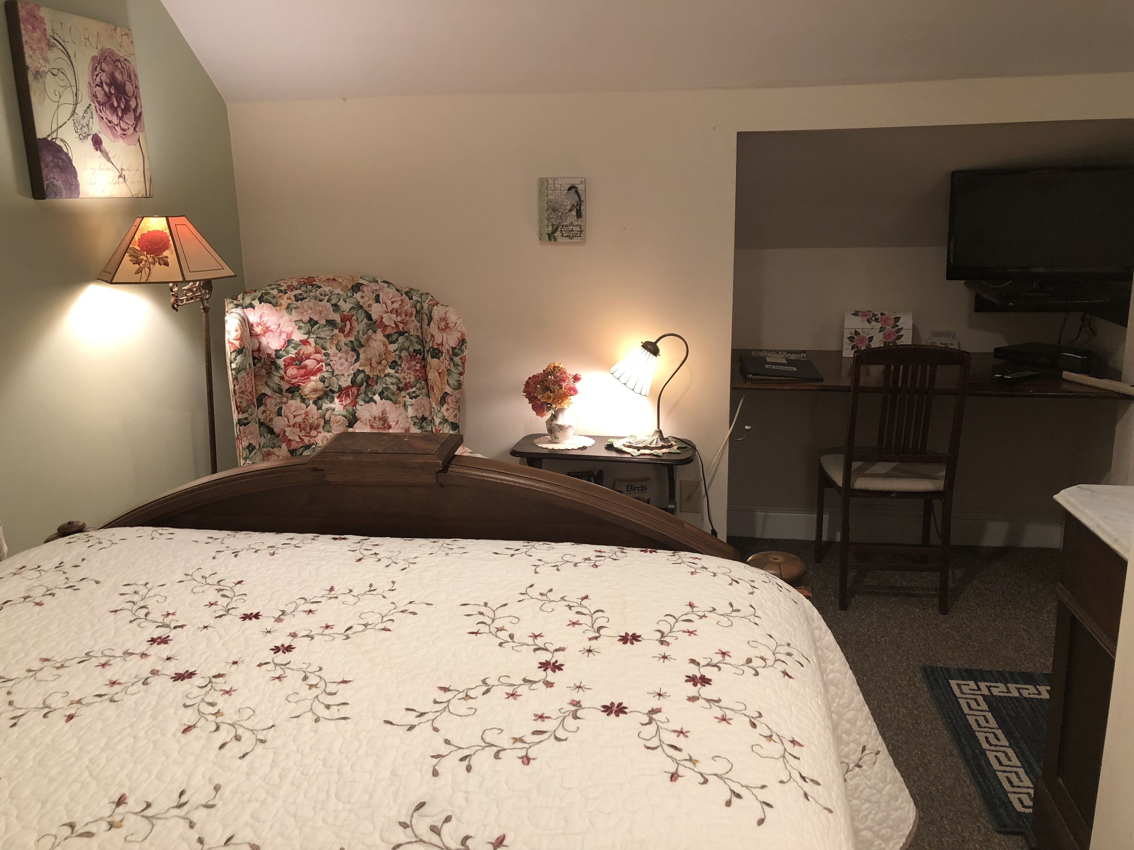 Hotellihuone, jossa on sänky, työpöytä, tuoli, televisio ja lamppu.