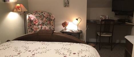 Hotellihuone, jossa on sänky, työpöytä, tuoli, televisio ja lamppu.