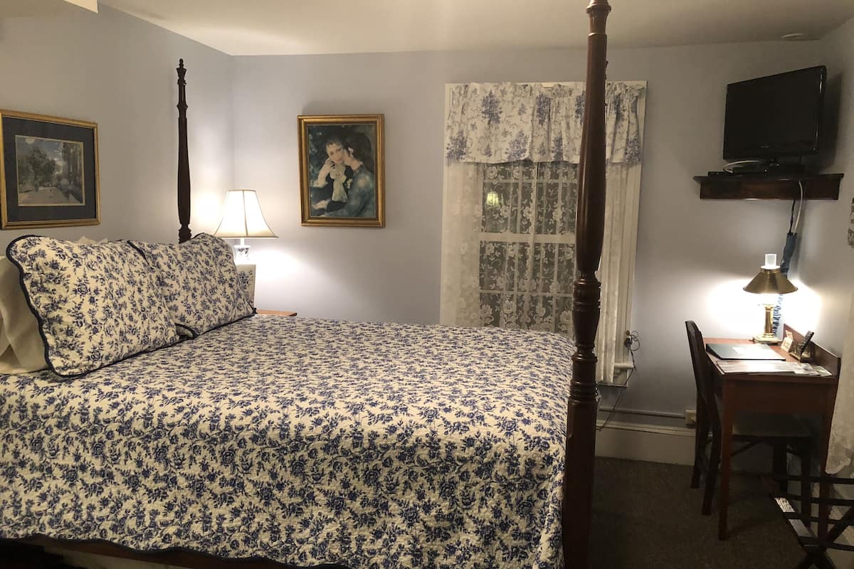 A bedroom with a four-poster bed, a desk with a chair, a television, and two framed pictures on the wall.