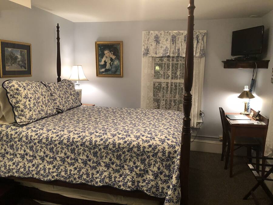 Un dormitorio con cama con dosel, un escritorio con silla, un televisor y dos cuadros en la pared.