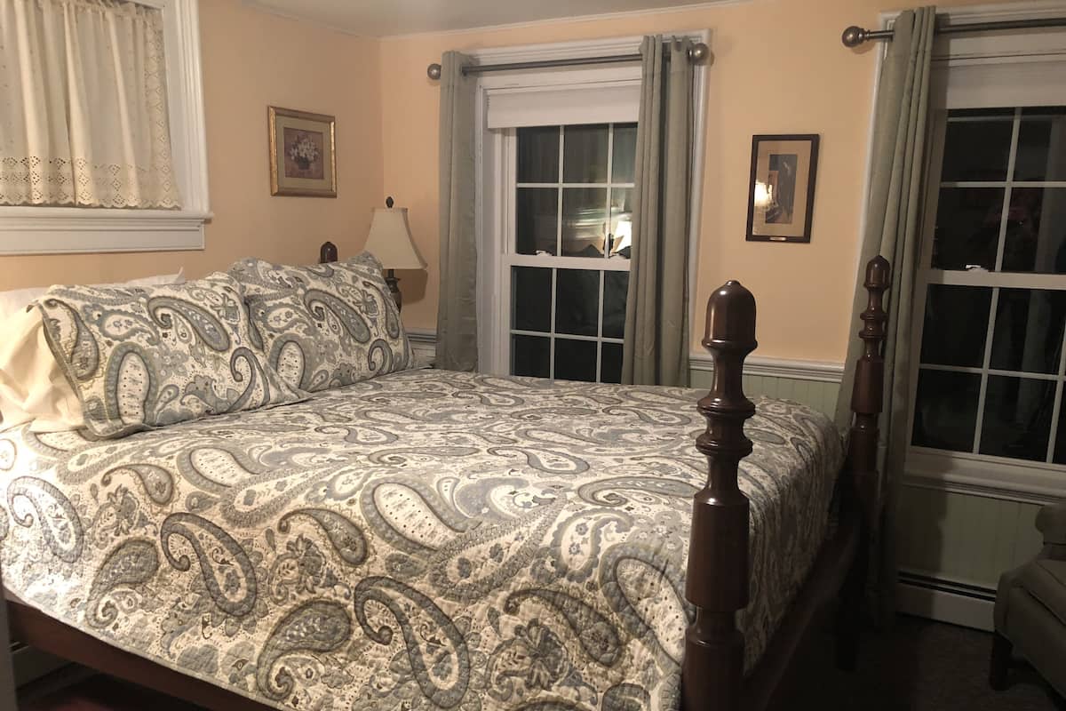 A bedroom with a bed, a nightstand, a lamp, and two windows with curtains.