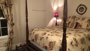 Ein Bett mit Baldachin, floraler Bettwäsche, einer Nachttischlampe und einem Wandbild in einem Rahmen.
