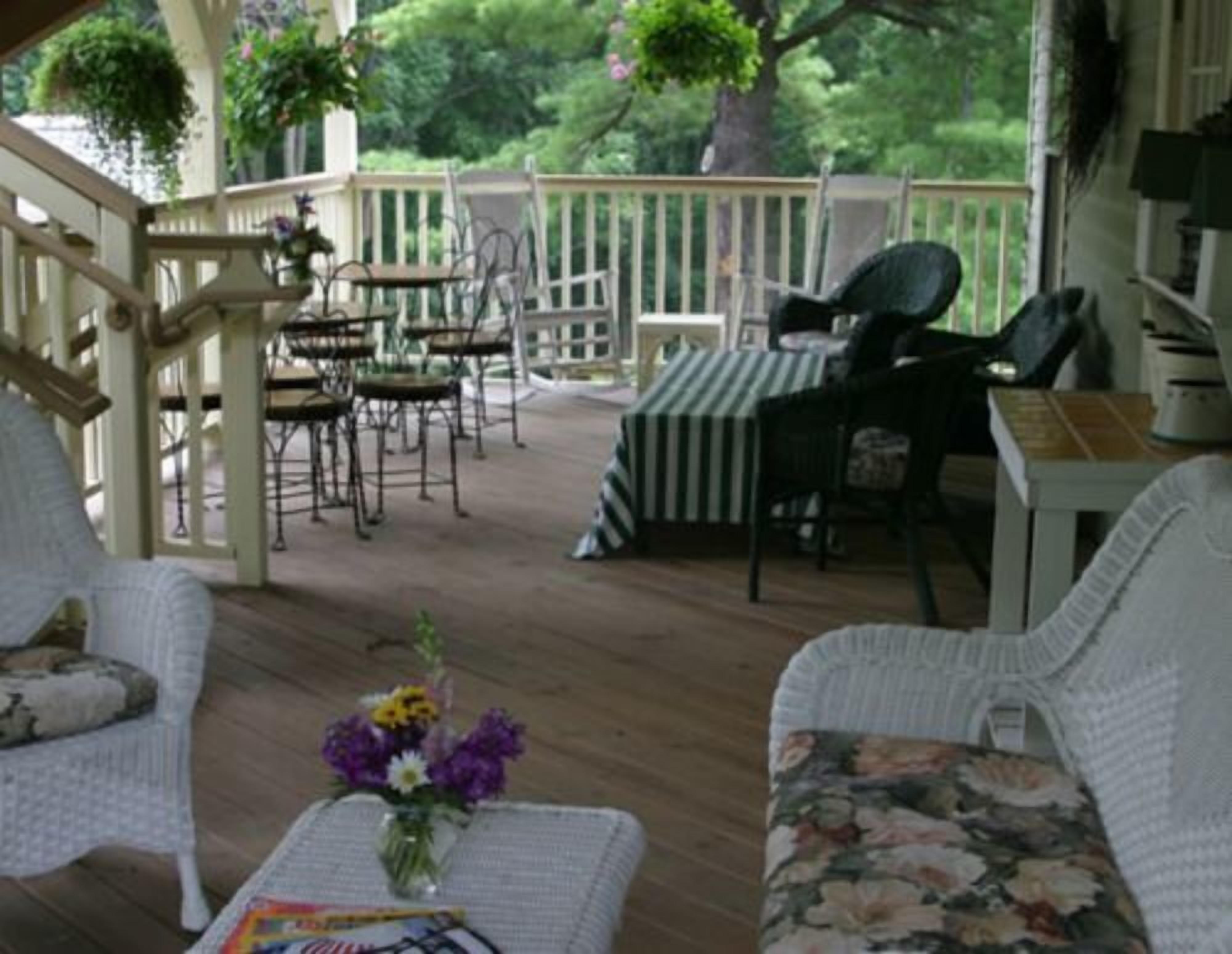 A covered outdoor seating area with wicker furniture, a table with a striped tablecloth, and a vase of flowers.