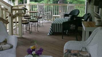 A covered outdoor seating area with wicker furniture, a table with a striped tablecloth, and a vase of flowers.