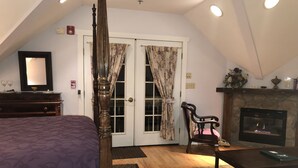 A bedroom with a four-poster bed, a fireplace, a wooden table, and a chair. - Alpine Haus Bed & Breakfast Inn (Vernon)