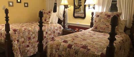A room with two wooden beds with floral quilts, a mirror, and two wall-mounted lamps.