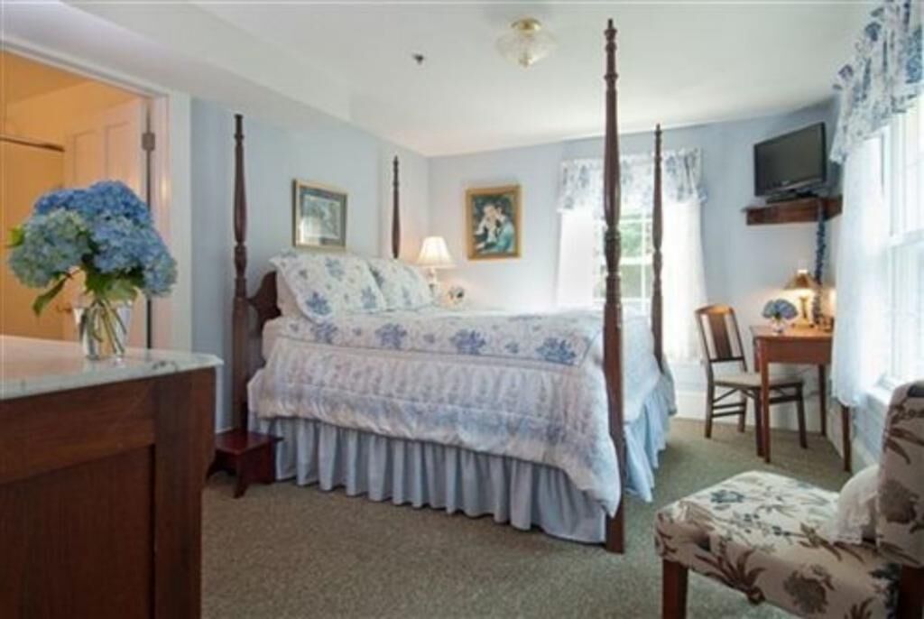 A bedroom with a four-poster bed, a desk with a chair, and a television on a shelf.