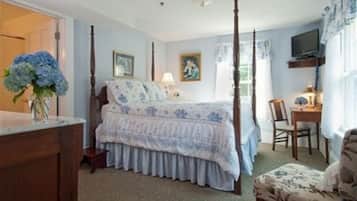 A bedroom with a four-poster bed, a desk with a chair, and a television on a shelf.