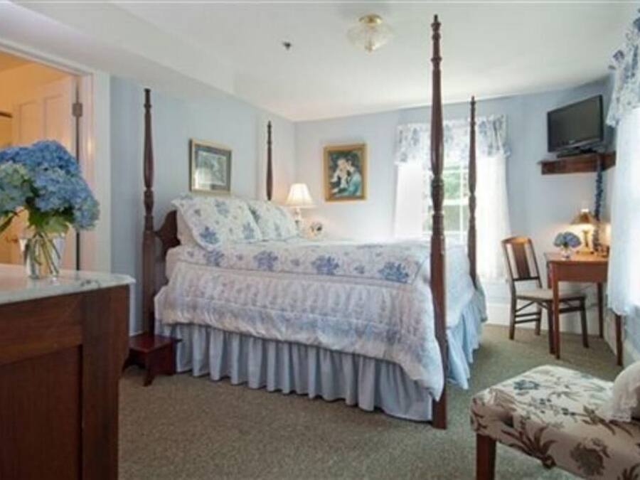 A bedroom with a four-poster bed, a desk with a chair, and a television on a shelf.