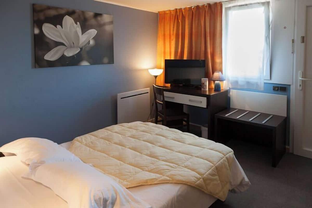 A hotel room with a bed, a desk with a computer, a lamp, and a window with curtains.