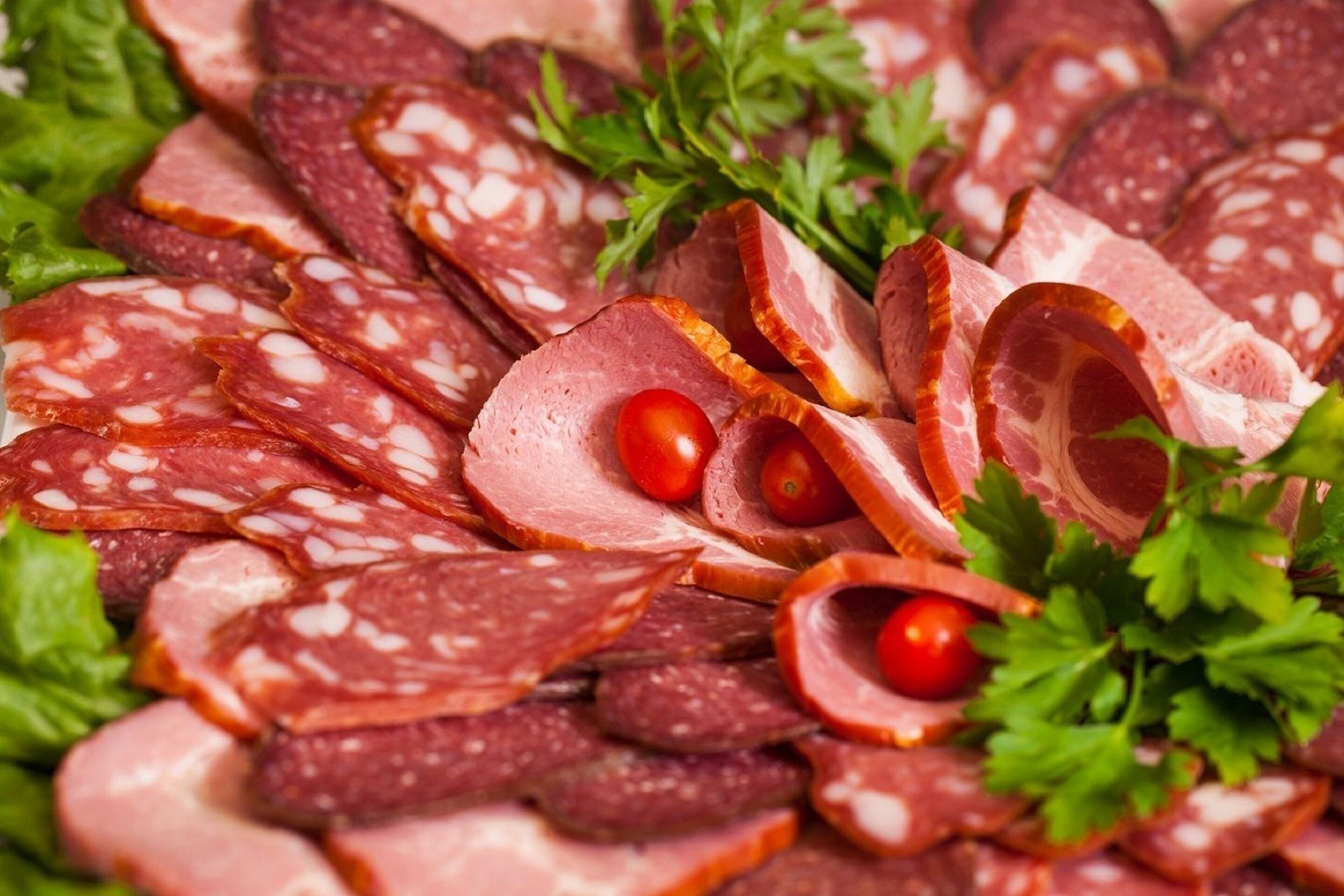 Een verscheidenheid aan plakjes droge worst, waaronder salami en parmaham, gepresenteerd op een slaatje en versierd met peterselie en kerstomaatjes.