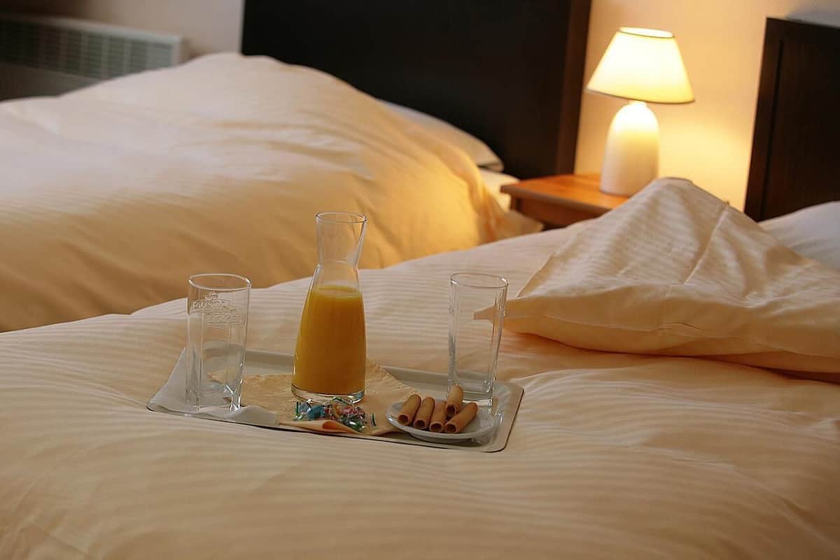 A neatly made bed with a tray of breakfast items including juice, a glass of water, and a plate of rolled oats.