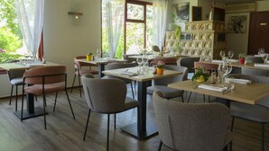 A dining area with multiple tables and chairs, a fireplace with decorative tiles, and large windows with curtains. - Au Relais D'Alsace (Rouffach)