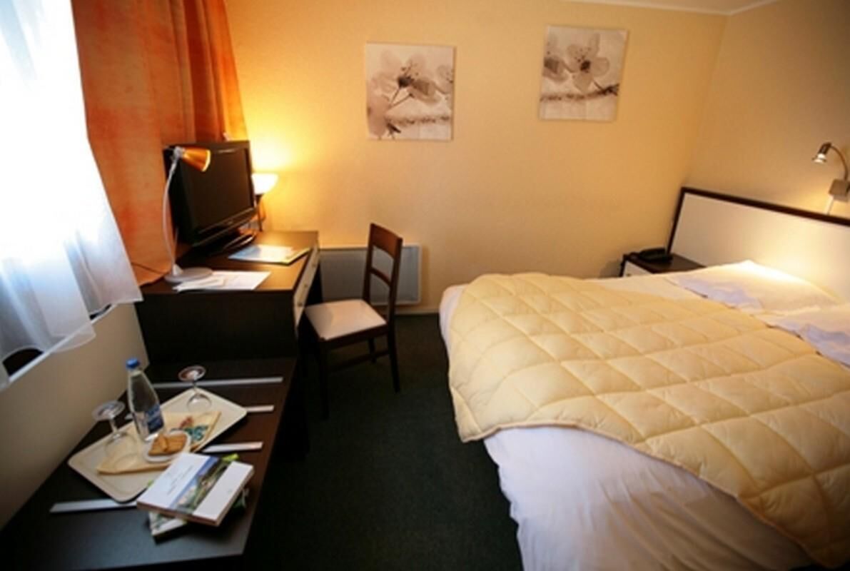 A hotel room with a bed, desk, chair, and two wall-mounted lamps.