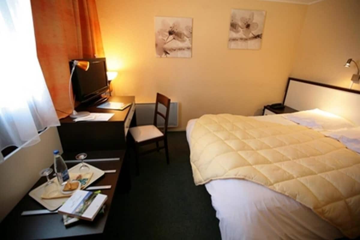 A hotel room with a bed, desk, chair, and two wall-mounted lamps.